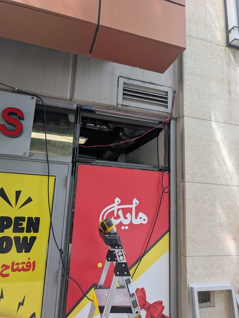 Glazier on a ladder fitting a new storefront panel above the entrance