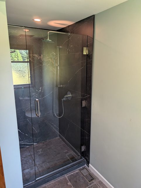 Frameless shower enclosure against dark marble walls with black hardware
