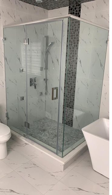 Frameless glass shower enclosure with chrome hardware and marble tile